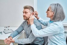 Doctor fitting the-Ear hearing aid into patient's ear while consultation in audiology clinic.